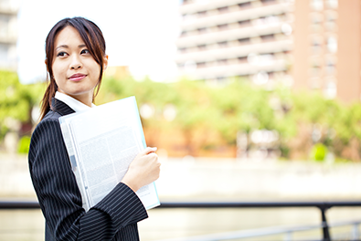 スーツの女性が外で書類を持って立っている